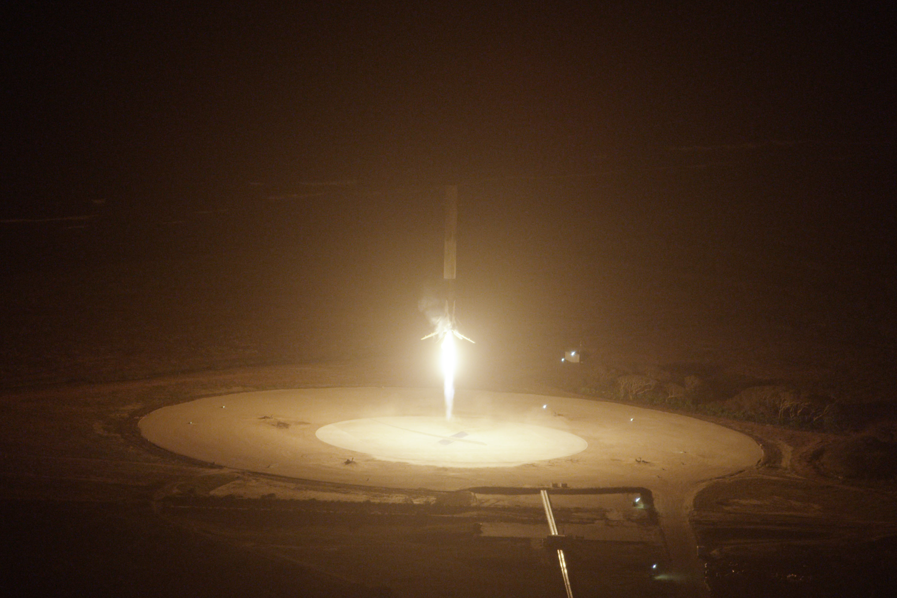 A SpaceX Falcon 9 first stage descends on a bright plume toward Landing Zone 1 during the first successful booster landing in December 2015.
