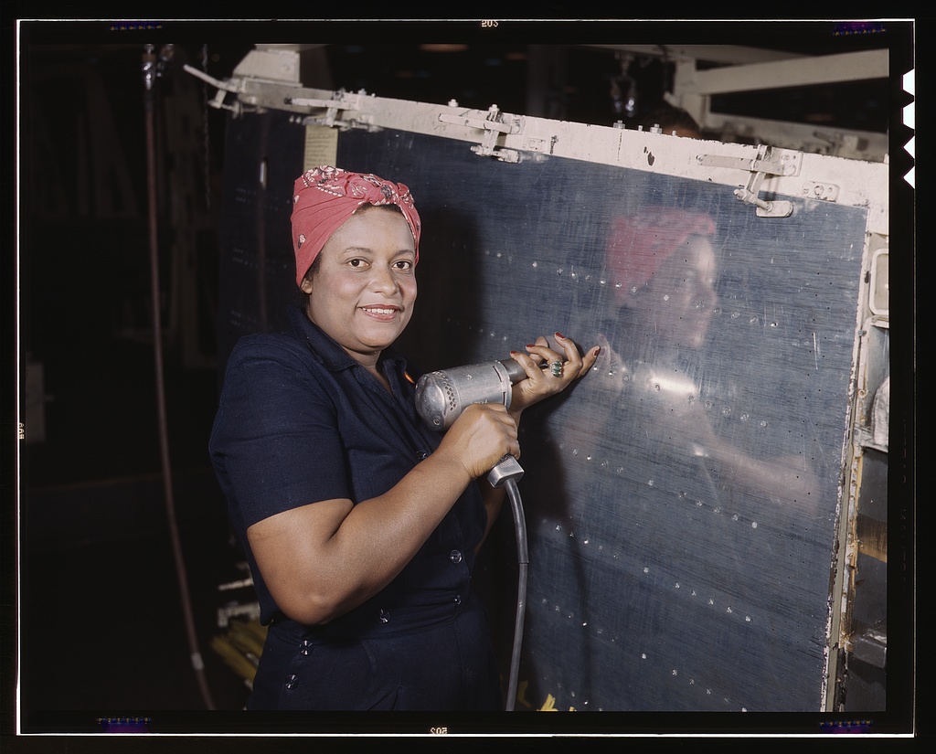 A woman aircraft worker wearing a red bandanna operates a hand drill at the Vultee Nashville plant in February 1943.